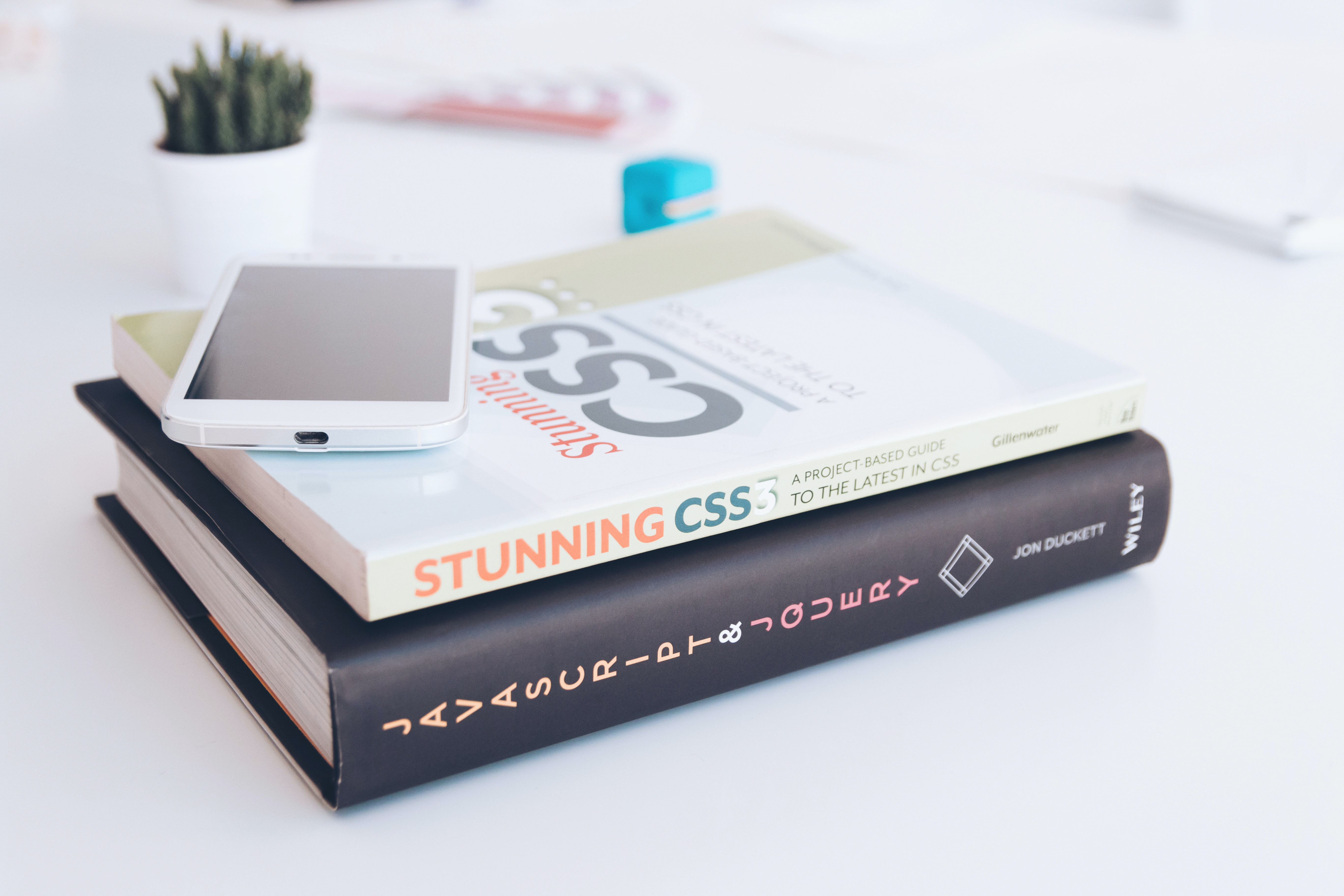 Photograph of a stack of two books on CSS, set on a white table. A cell phone sits on top of the books.